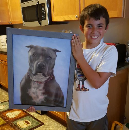 Boy holding framed painting of pit bull terrier.
