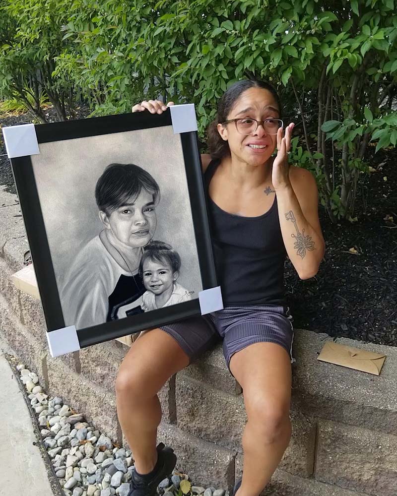 Woman crying while holding framed portrait of older woman and child.