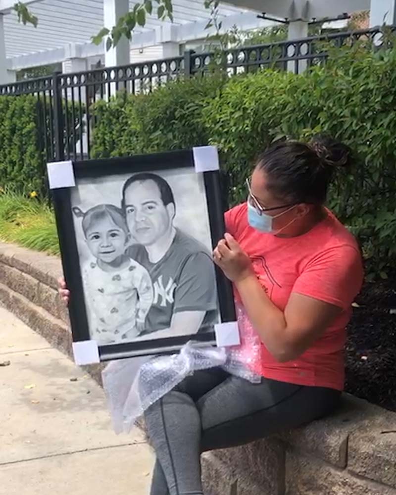Woman outdoors holding framed portrait of man and toddler.