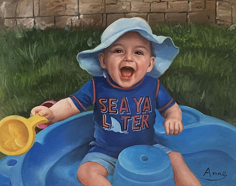 Laughing baby in blue hat and shirt, playing in blue plastic pool with yellow scoop.