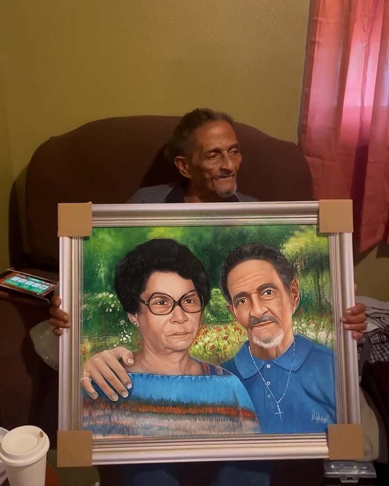 Elderly man holding framed portrait of older couple.