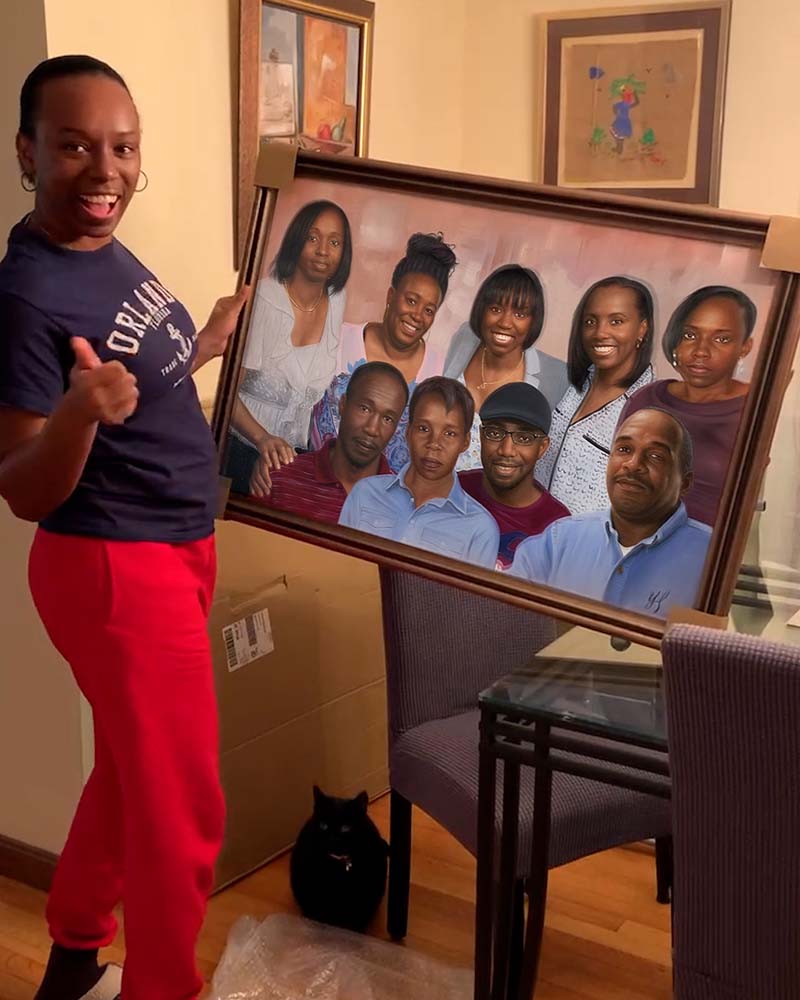 Woman holding large framed family portrait, giving thumbs up.