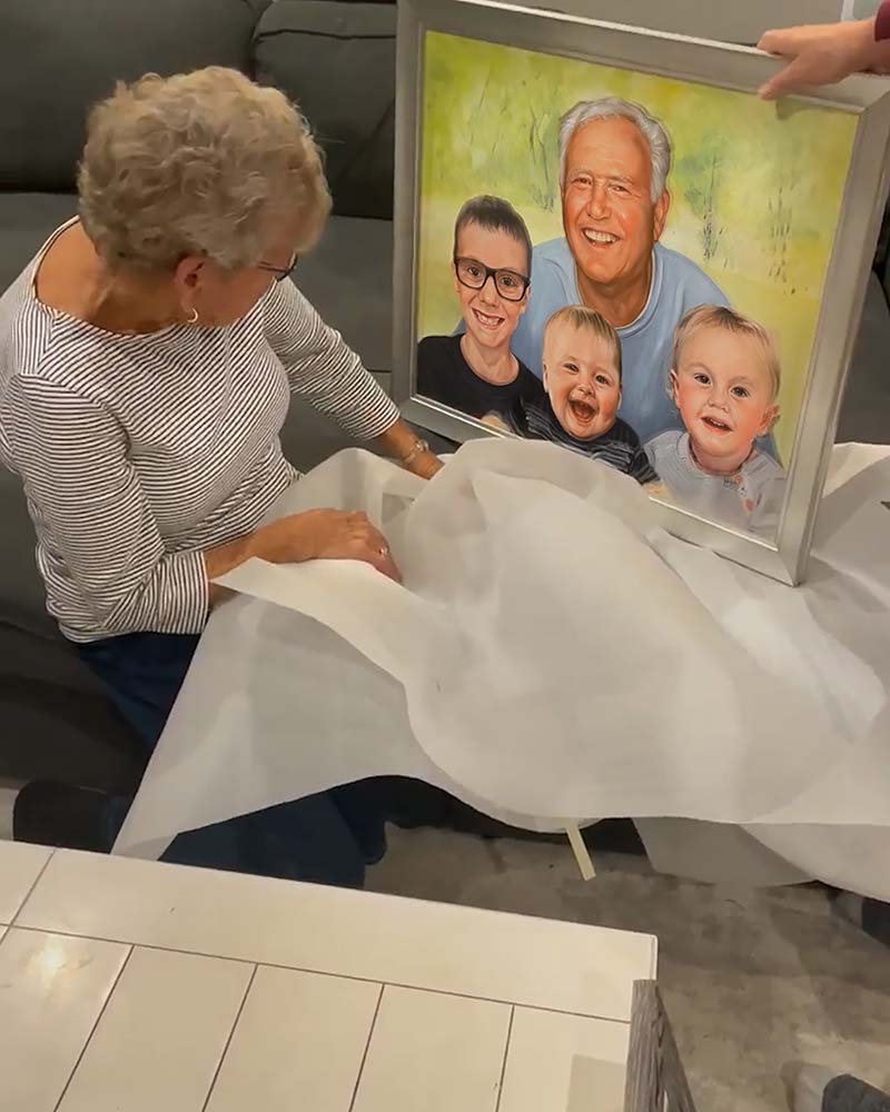 Woman unveiling framed family portrait of grandfather and two grandsons.