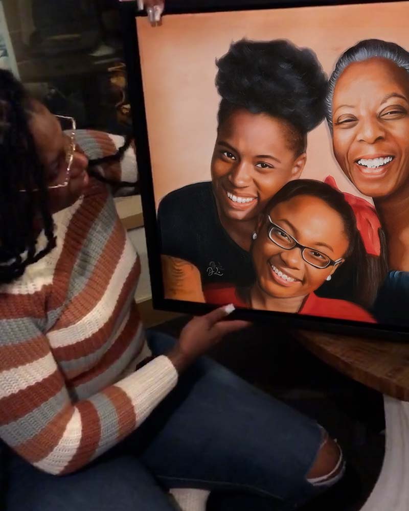 Woman holding framed portrait of three generations of Black women.
