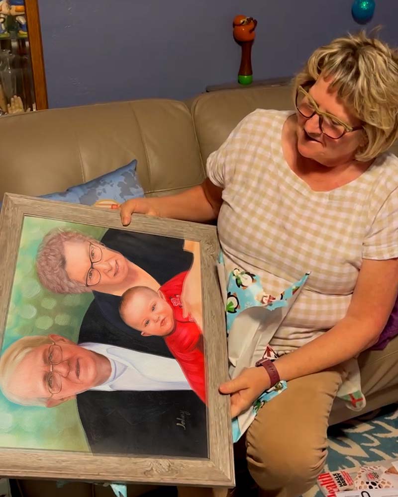 Woman holding framed portrait of grandparents and baby.