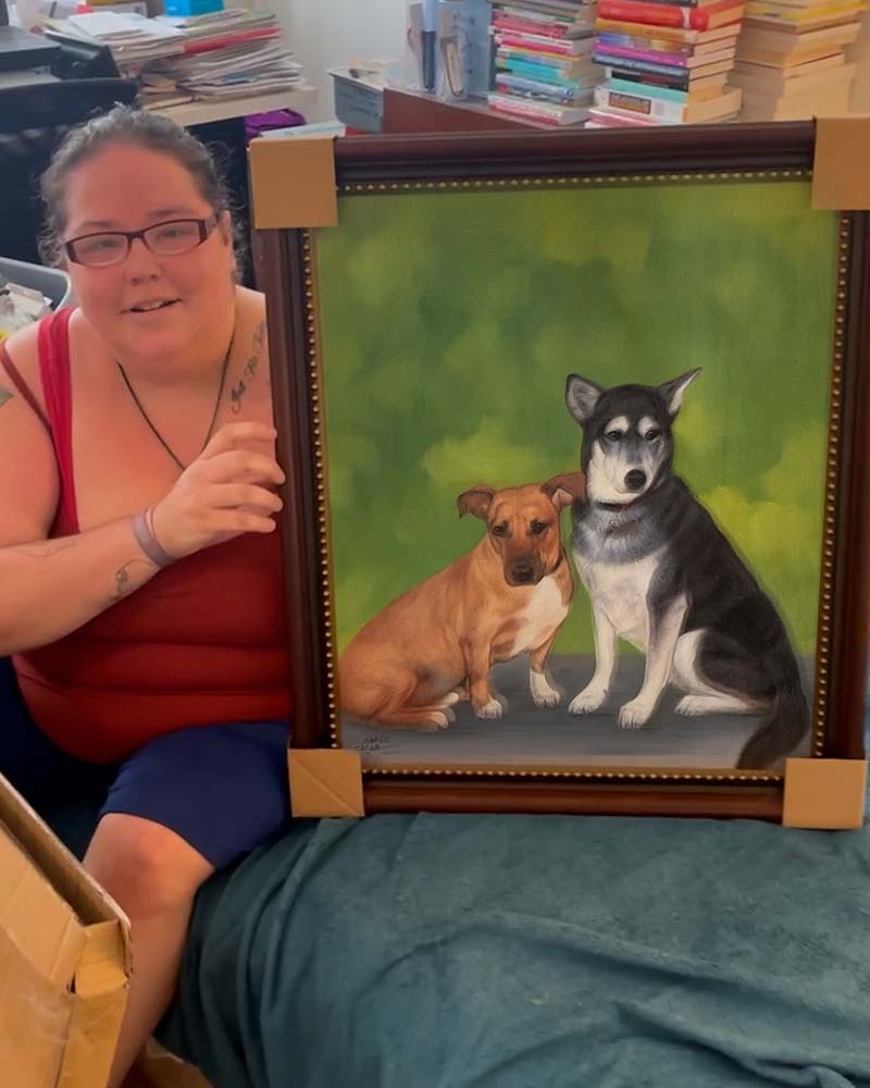 Woman holding framed painting of two dogs.