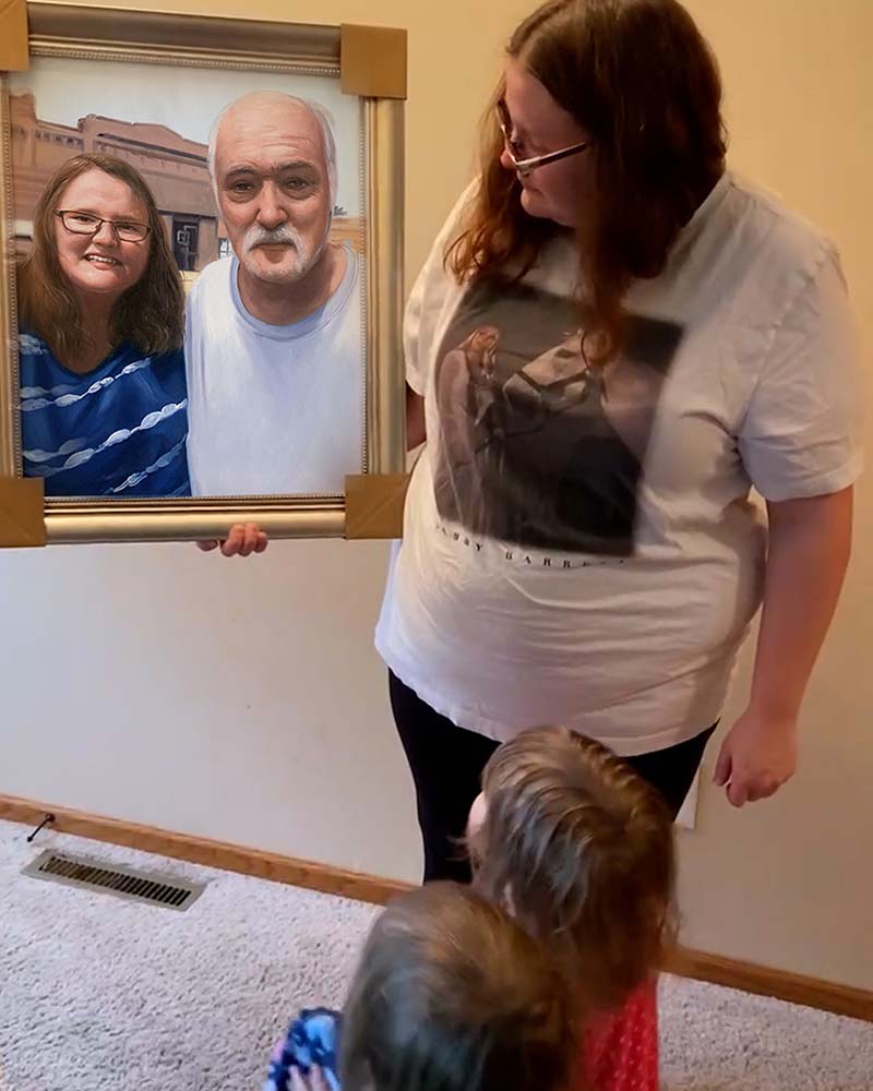 Woman holding framed portrait of older couple with two young children looking on.