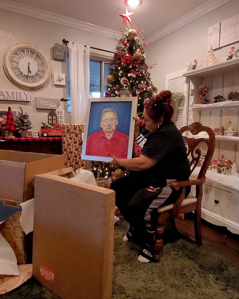Woman holding framed portrait in front of Christmas tree.