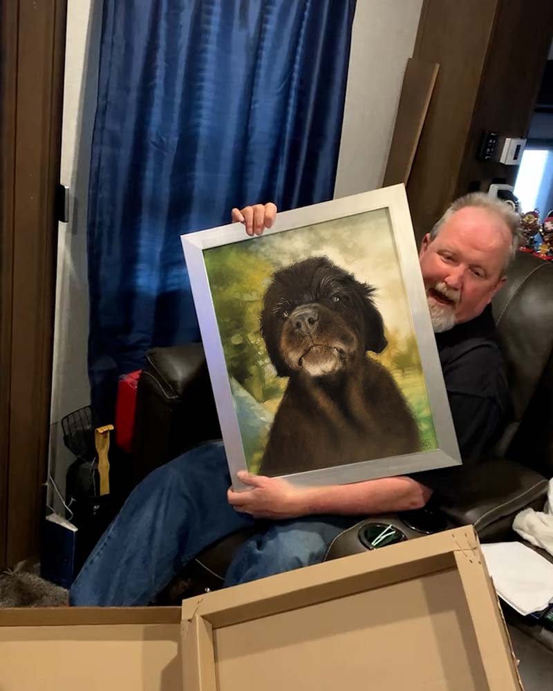 Smiling man holding framed painting of dark brown dog.