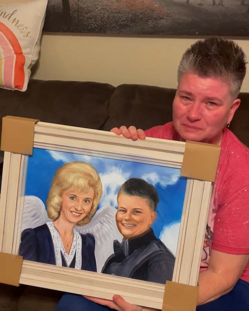 Woman crying while holding framed portrait of two women, one with angel wings.