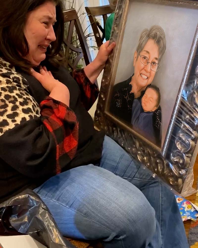 Woman crying while holding a framed portrait of an older woman holding a baby.