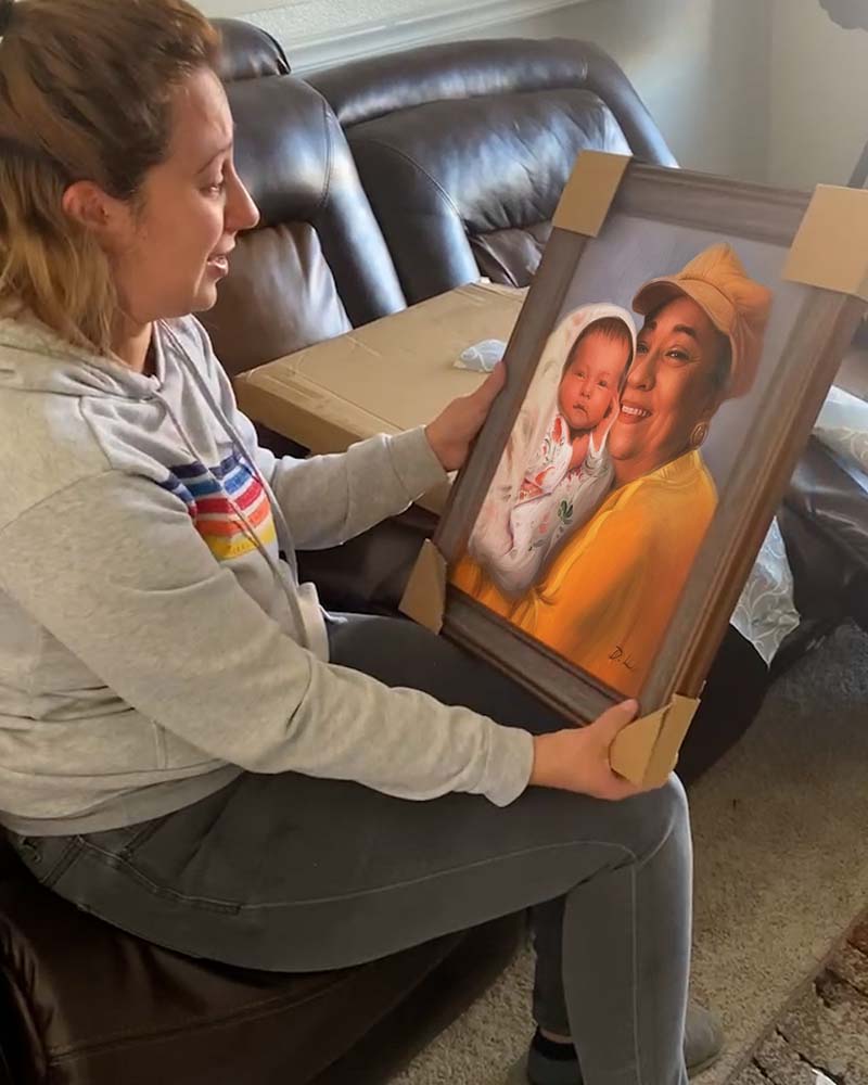 Woman holding framed portrait of grandmother and baby.
