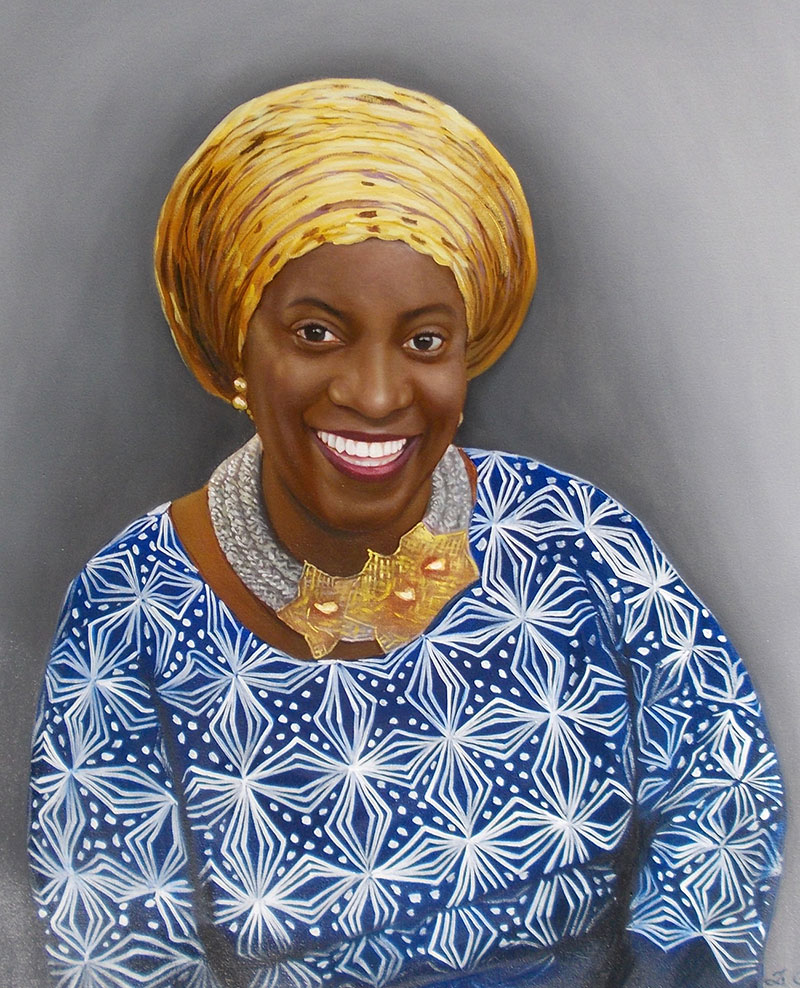 Portrait of a smiling Black woman wearing a yellow headwrap and blue patterned dress.