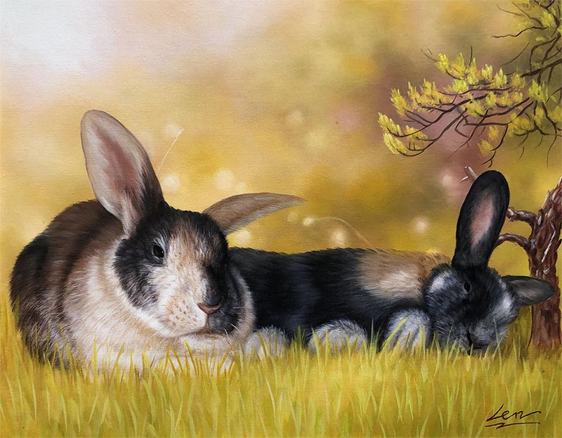 Two rabbits resting in grass near a small tree.