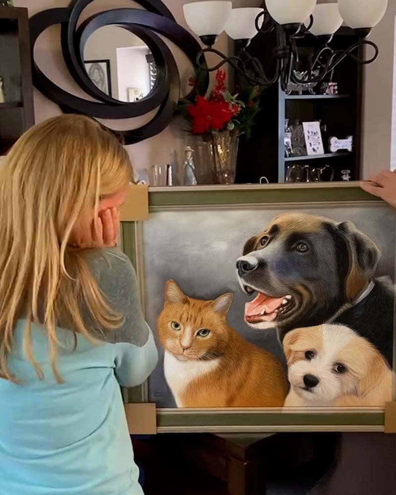 Woman admiring framed pet portrait of cat and two dogs.