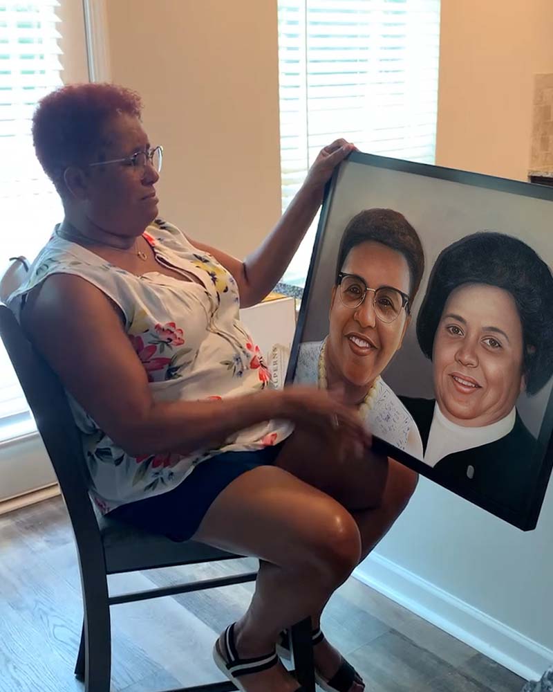 Woman seated, holding a framed portrait of two women.