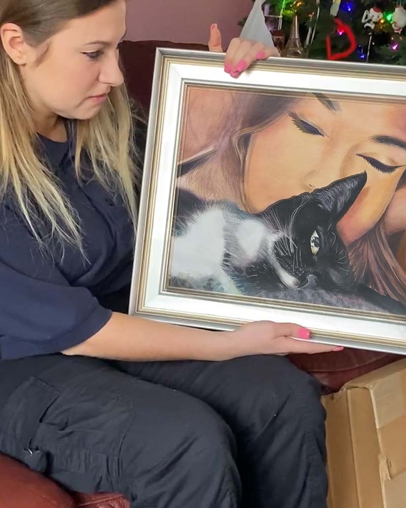 Woman holding framed portrait of herself and cat.