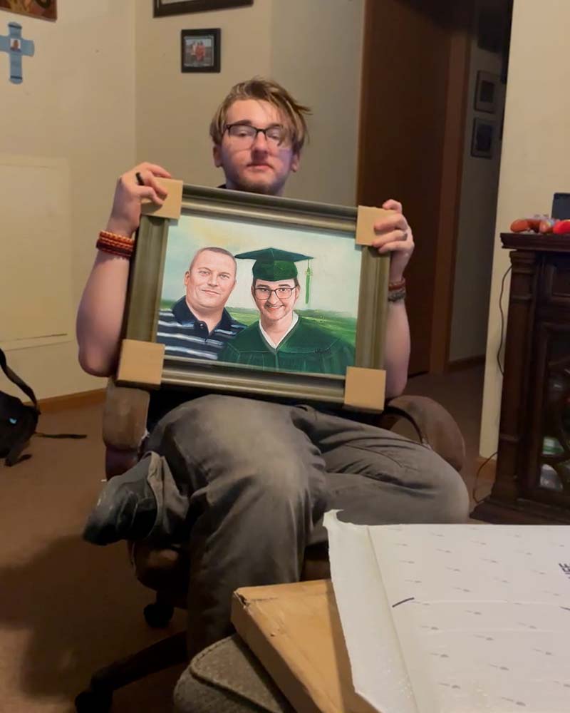 Person holding framed portrait of two men, one in graduation gown.
