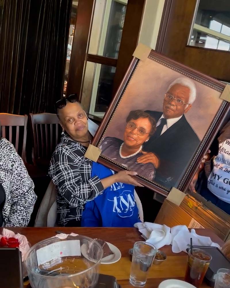 Woman holding framed portrait of elderly couple at restaurant table.