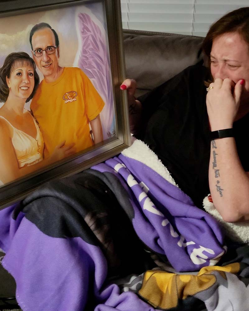 Woman crying while holding a framed portrait of a couple with angel wings.
