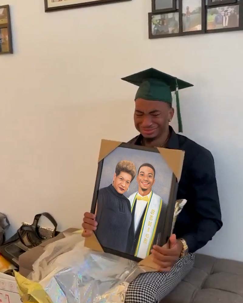 Graduate in cap and gown crying while holding a framed portrait of himself and a woman.