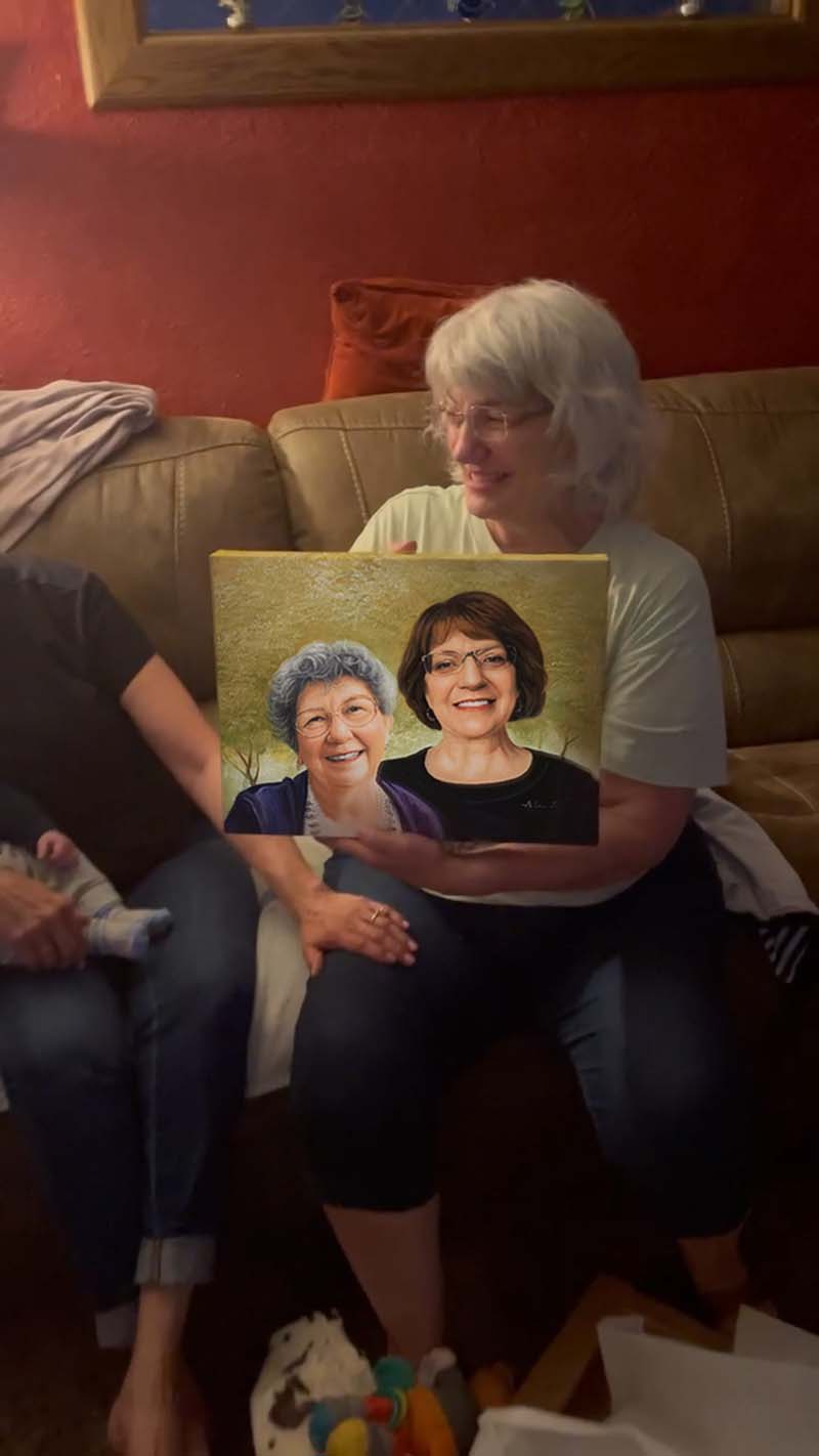 Woman holding a painted portrait of two women on a canvas.