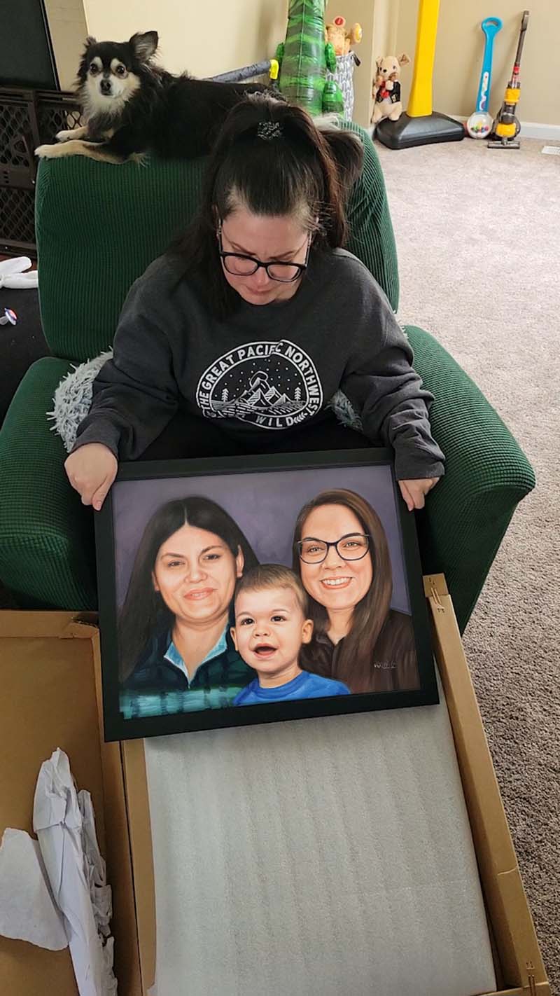 Woman holding framed portrait of two women and a toddler, small dog on back of chair.