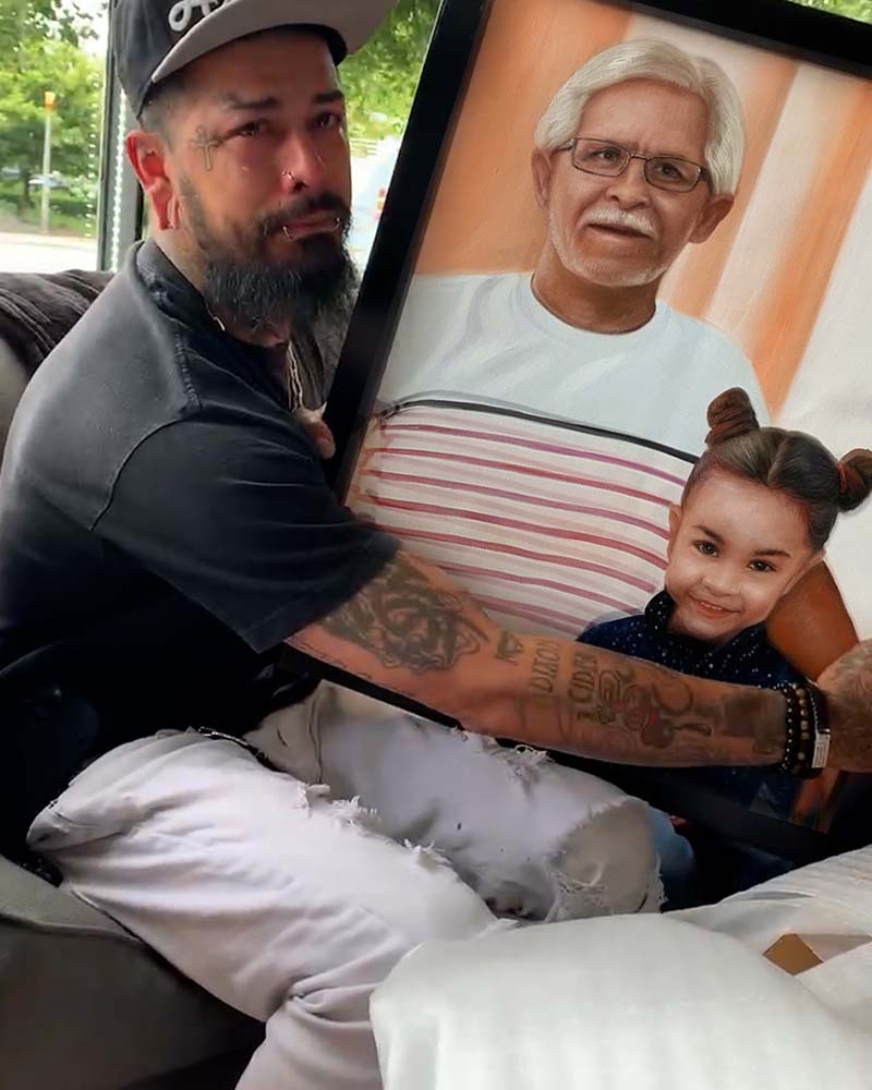 Man holding framed portrait of elderly man and young girl, crying.