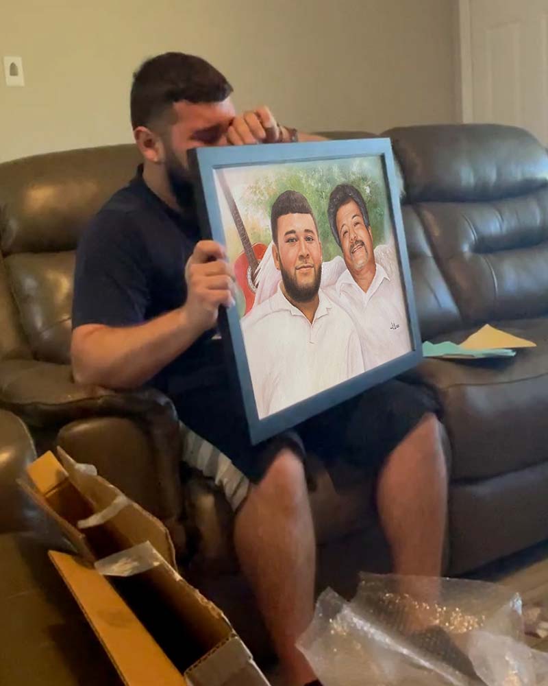 Man crying while holding framed portrait of two men.