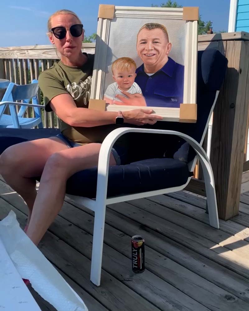 Woman holding framed portrait of man and toddler on deck.