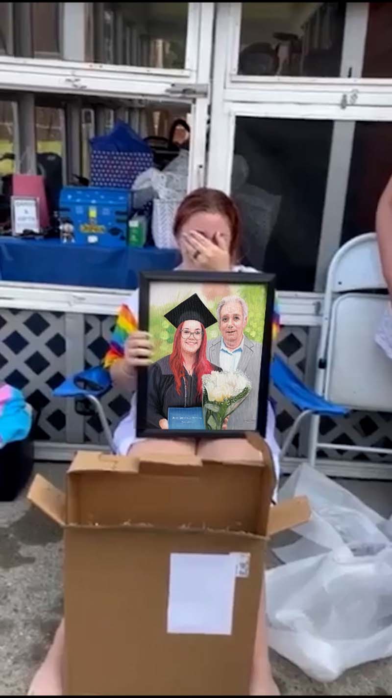 Person crying while holding a framed portrait of a graduate and an older man.