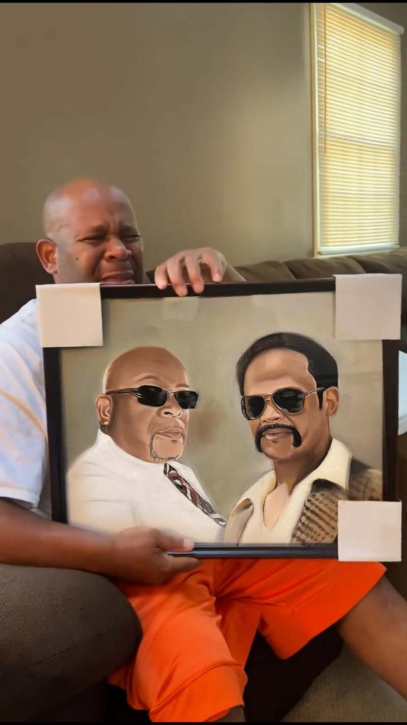 Man holding framed portrait of two men in sunglasses.