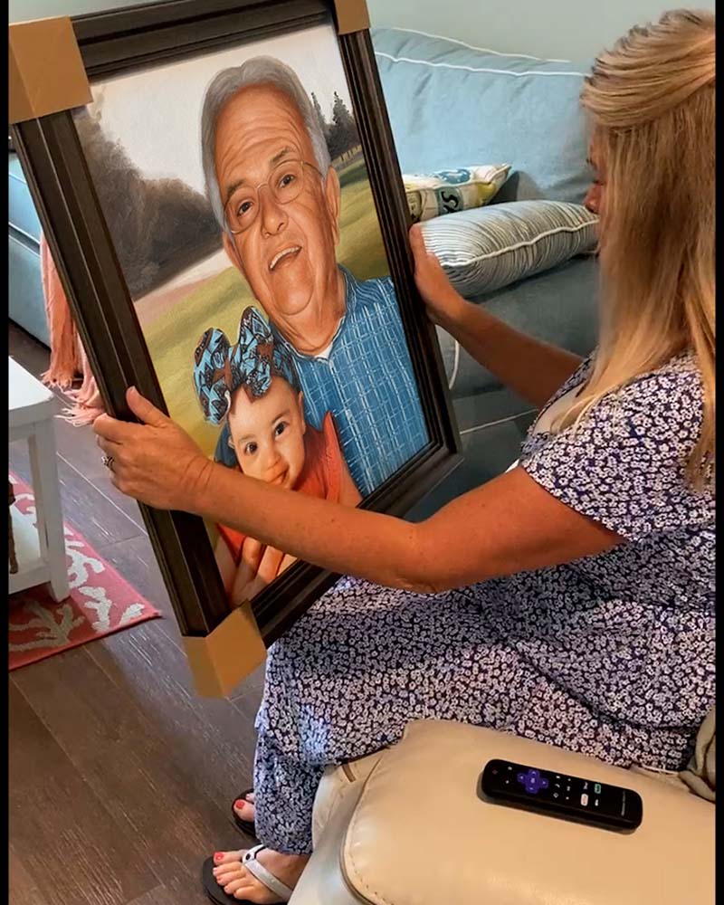 Woman holding framed portrait of grandfather and baby.
