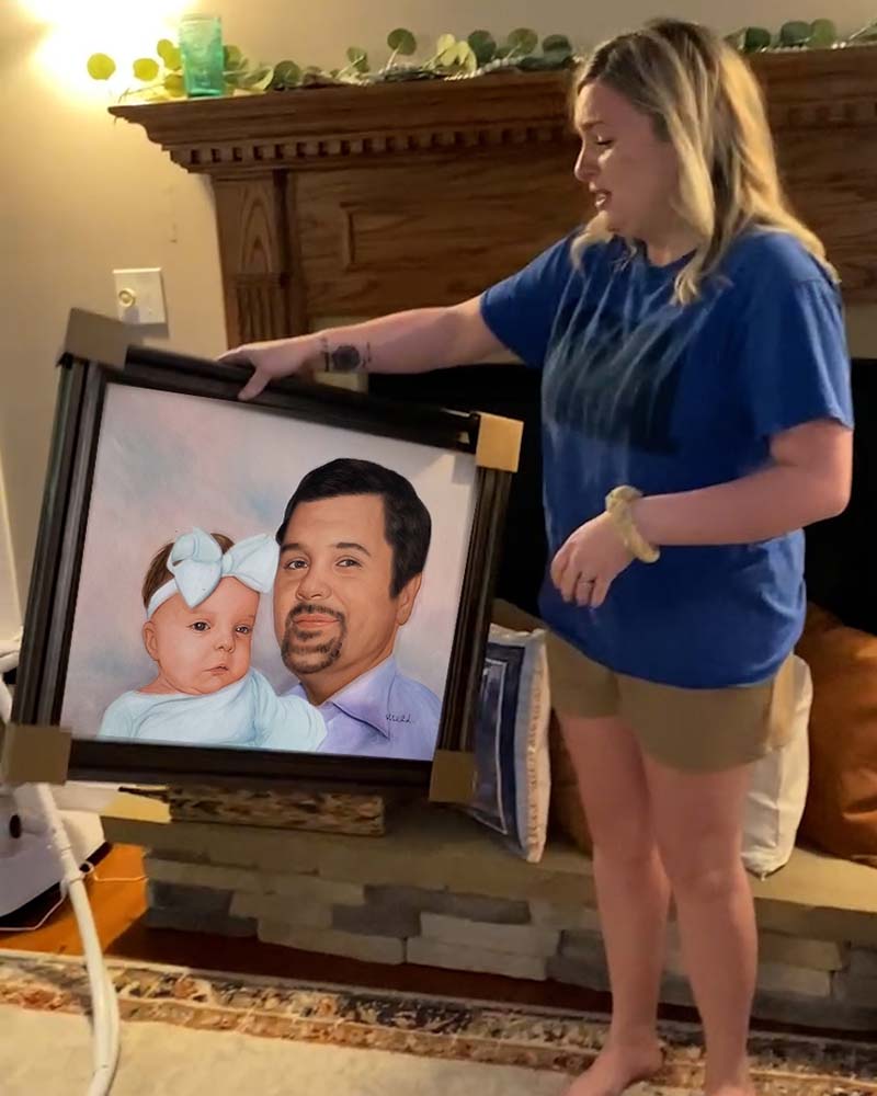 Woman holding framed portrait of man and baby.