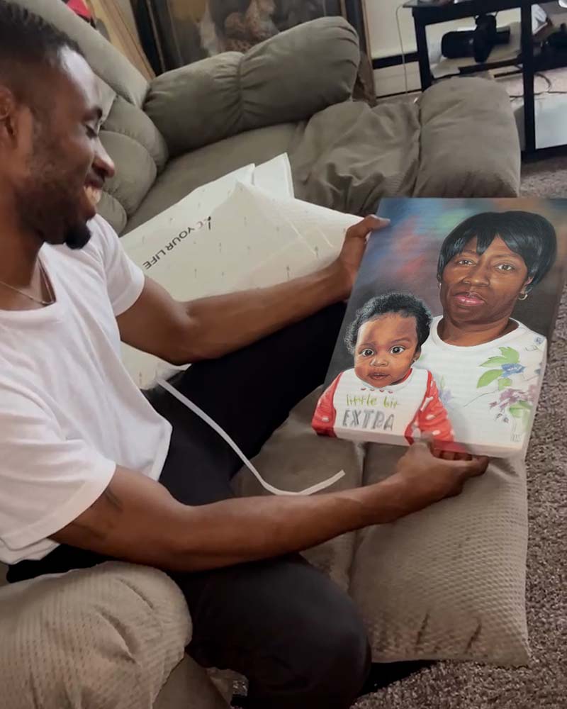 Man smiling while holding a painted portrait of a woman and baby.