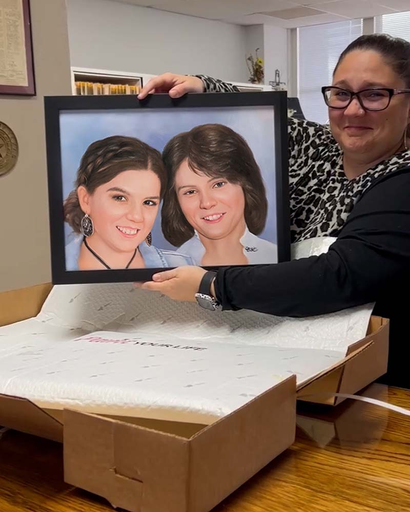 Woman holding framed portrait of two women, one younger and one older.