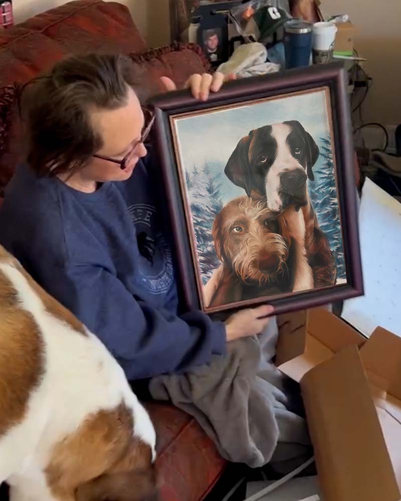Person holding framed painting of two dogs in winter setting.
