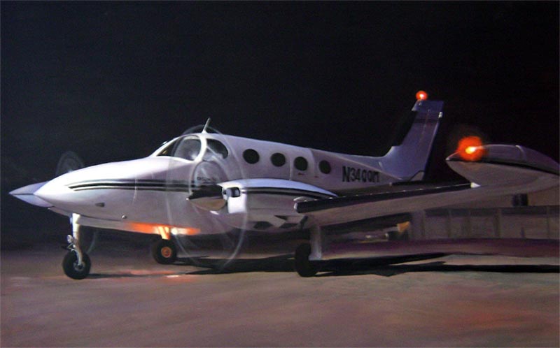 White twin-engine propeller plane on tarmac at night.